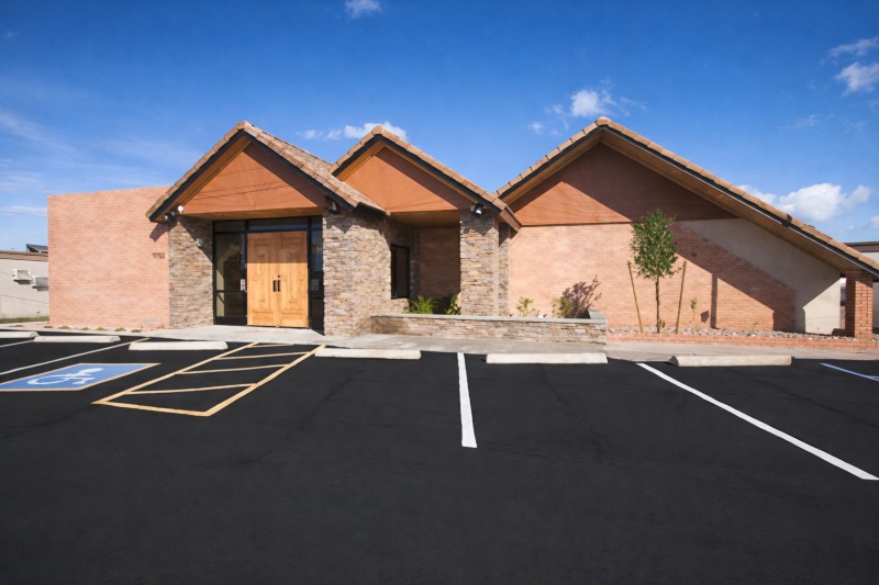 Direct Cremations Mesa, AZ facility exterior with stone facade, wood double doors and parking spaces.
